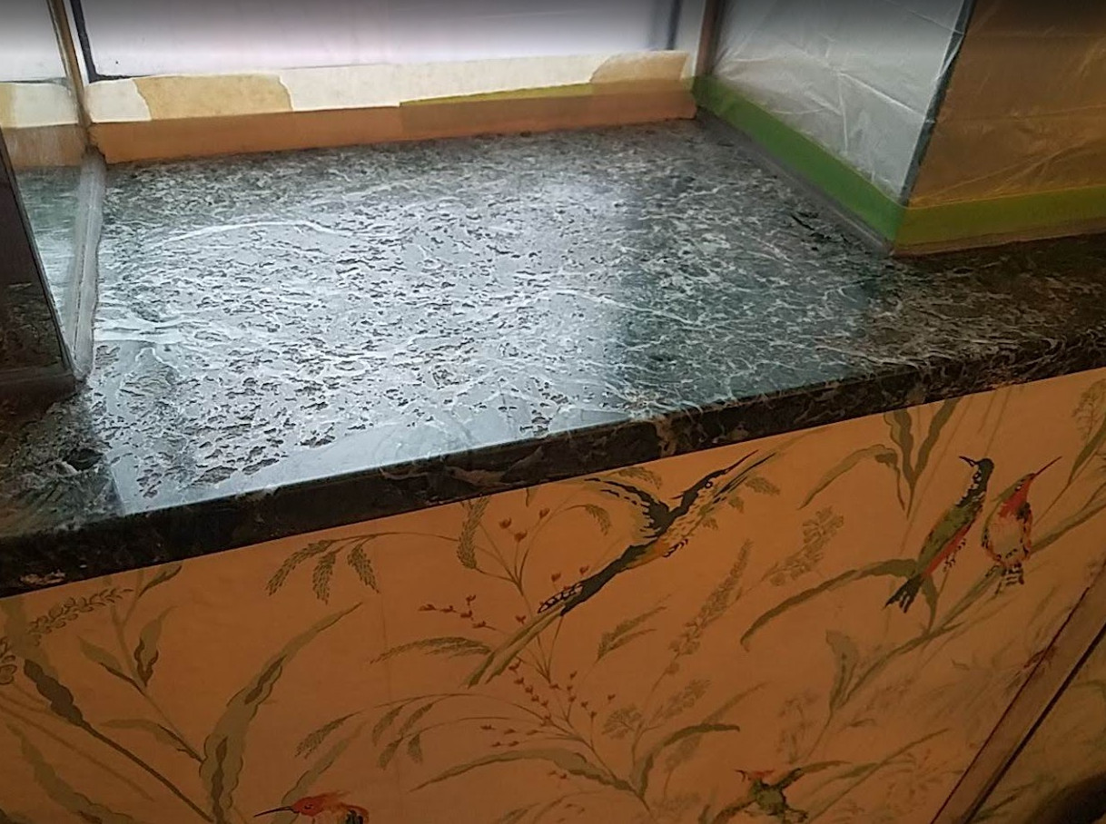 Heavily pitted and weathered dark marble windowsill before polyester resin fill-in coating treatment