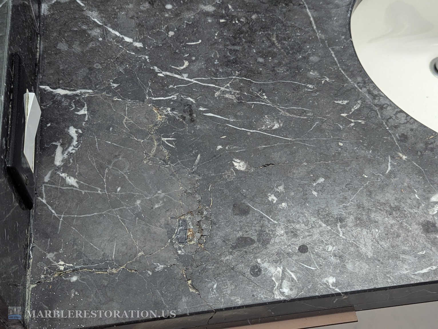 Cracks with loose pieces in a black marble vanity top before patching Close-up of cracks in black marble with small loose pieces, before patching with black epoxy