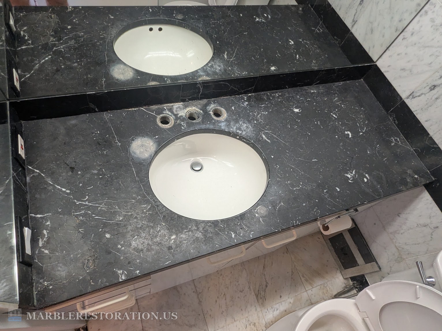 Black marble vanity top with dull gray spots before refinishing Black marble double sink vanity top with a gray dull haze and stains around the open faucet holes