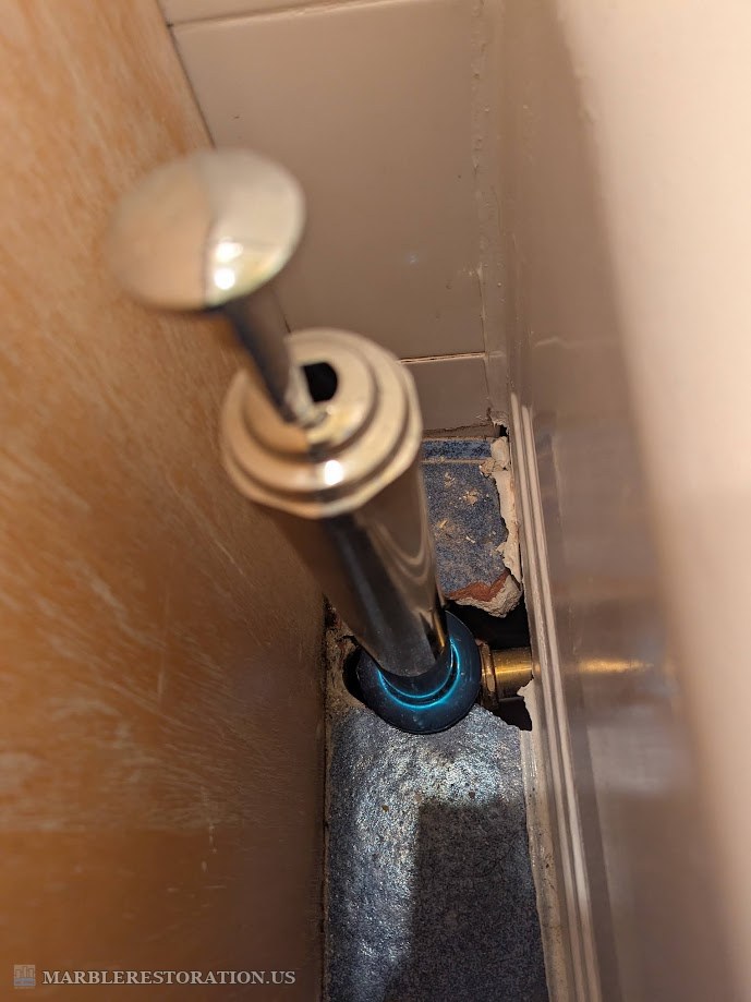 Broken blue ceramic floor tile and broken white wall tile next to a chrome tub overflow pipe, the floor open beside it