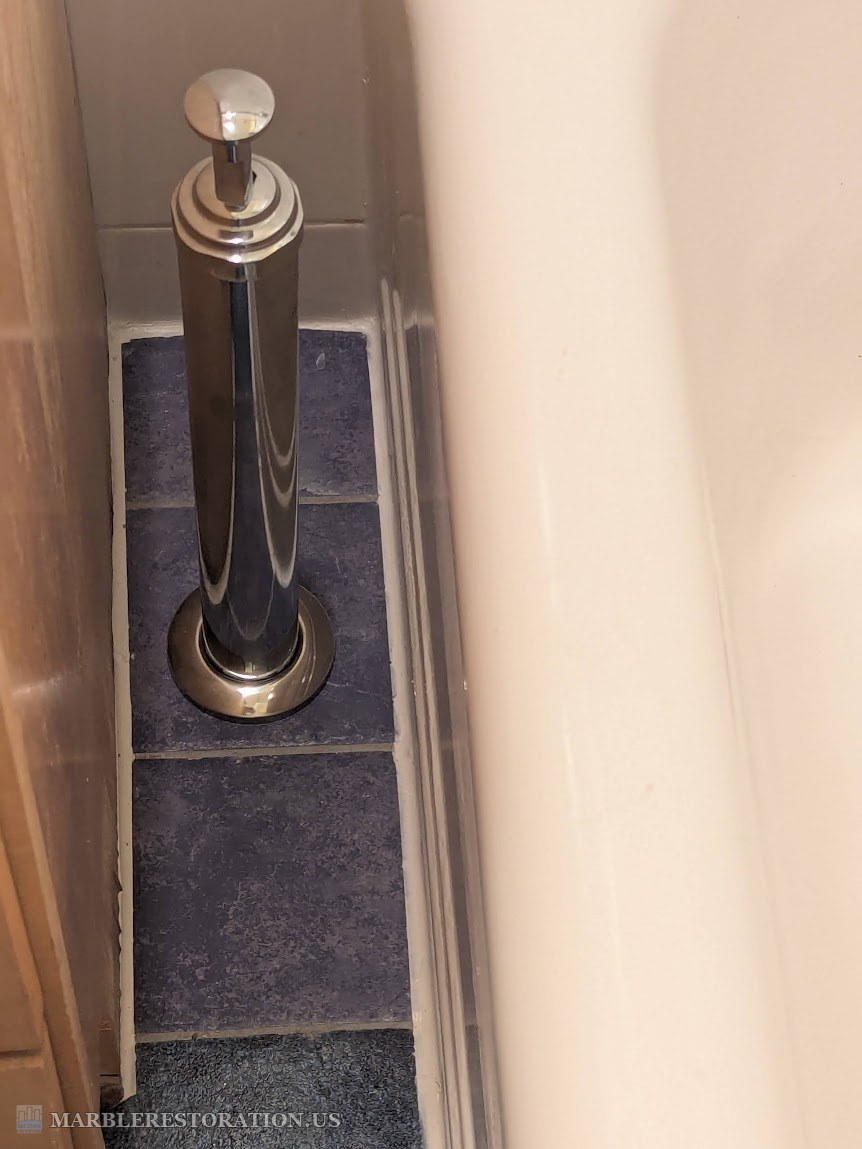 New matte blue floor tiles in a niche between a vanity and a bathtub, the chrome overflow pipe standing on the drilled tile