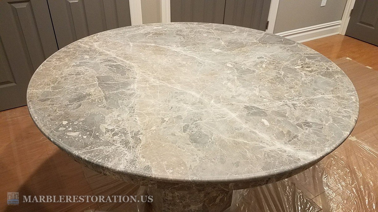 Emperador marble table with the old resin coating removed, before the new coat Round Emperador Dark marble table top indoors with the old coating removed, the bare marble dull and grey, plastic on the floor