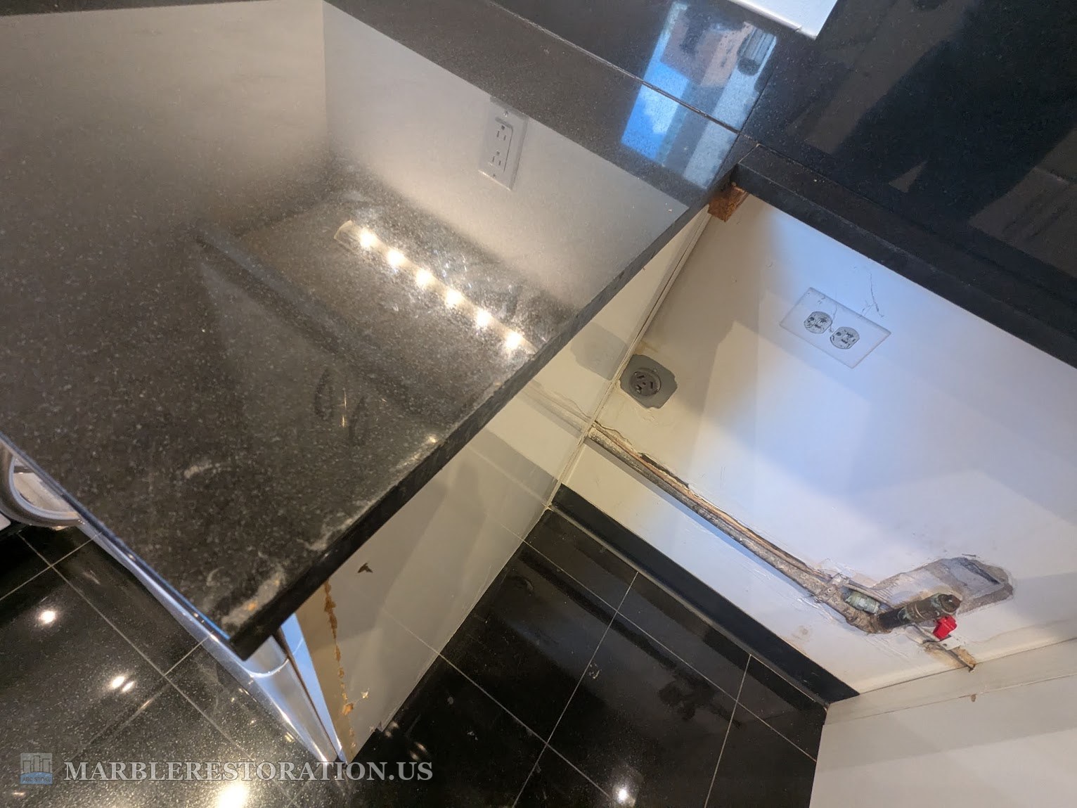 Left granite side at the stove gap, before the cut Black granite countertop at the left side of an empty stove gap, dust on the top, open wall with the gas pipe behind