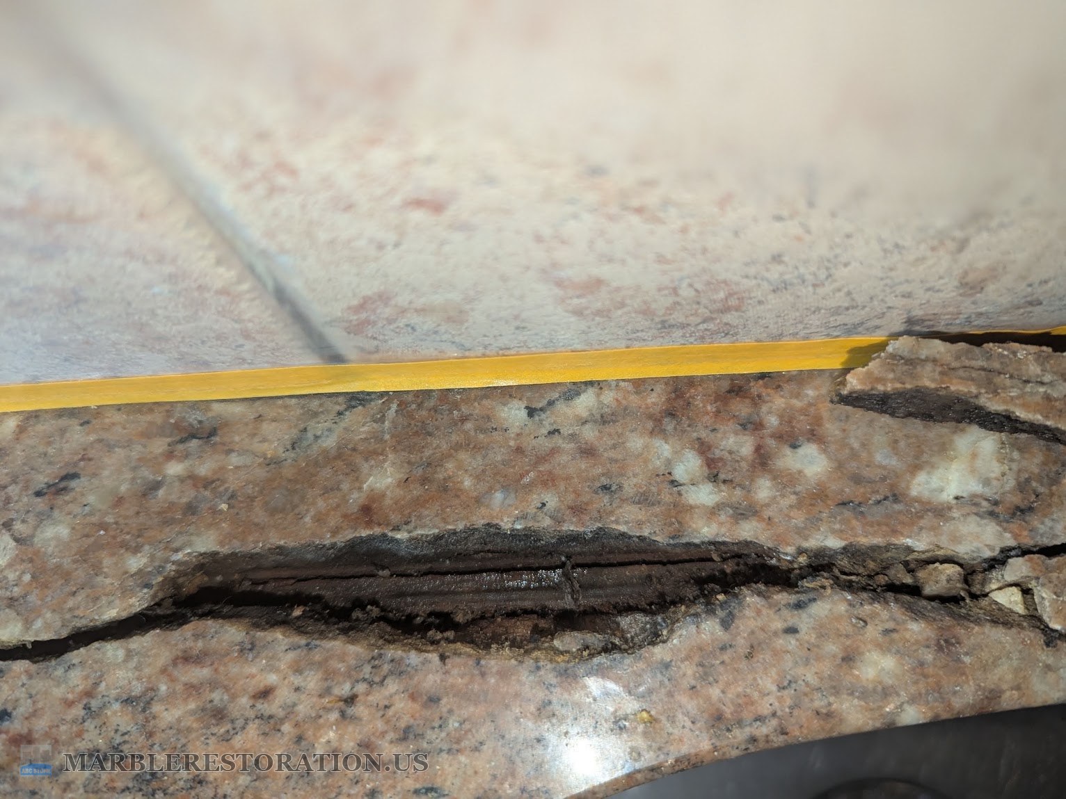 Close-up of an open crack in pink granite with a dark brown rusted metal rod inside it, wet with rust