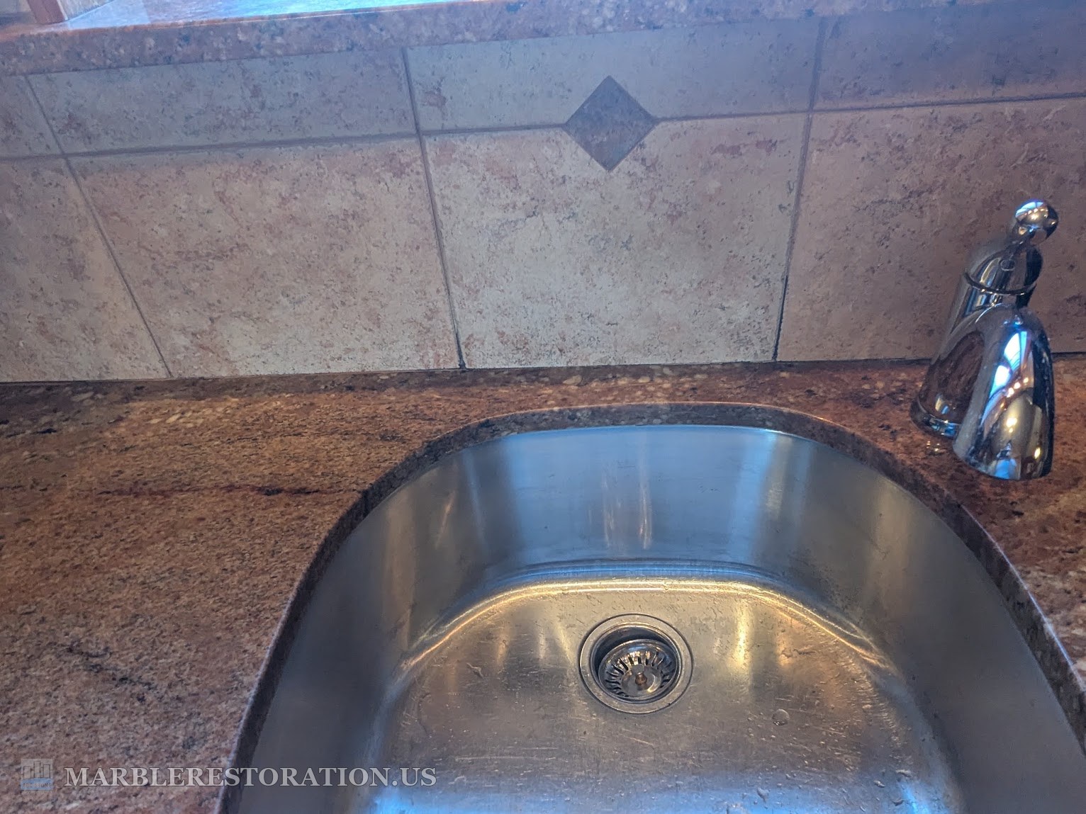Pink granite kitchen countertop behind an undermount stainless sink after the crack repair, tile backsplash and chrome faucet above it