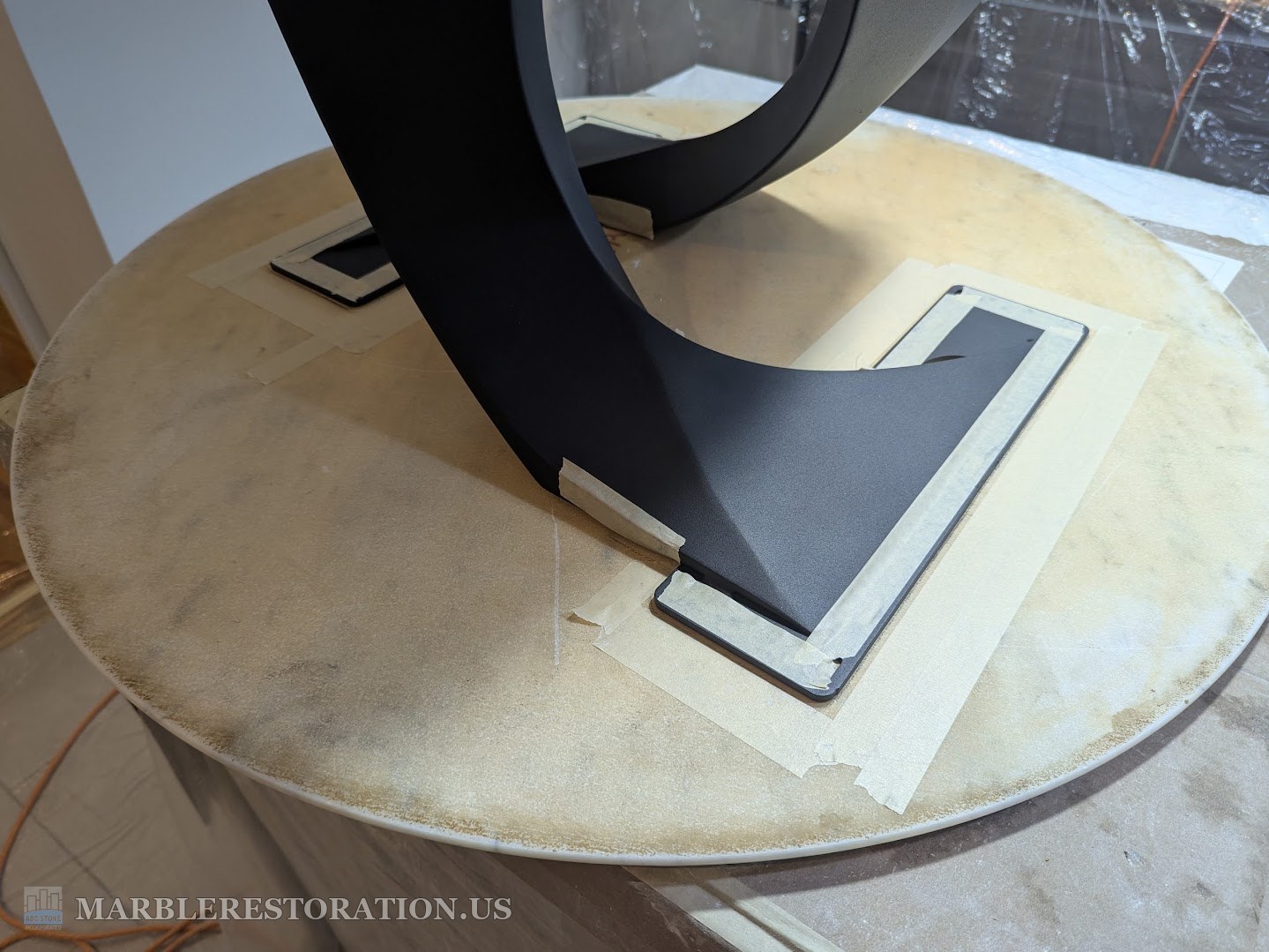 Marble coffee table top set on a new leg with clear silicone Marble table top upside down with the black leg set on its back side, tape around the plates