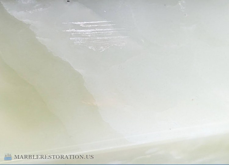 Scratches on an onyx furniture base Cluster of thin white scratches on the honed surface of a pale onyx furniture base, with a green vein running down the left side.
