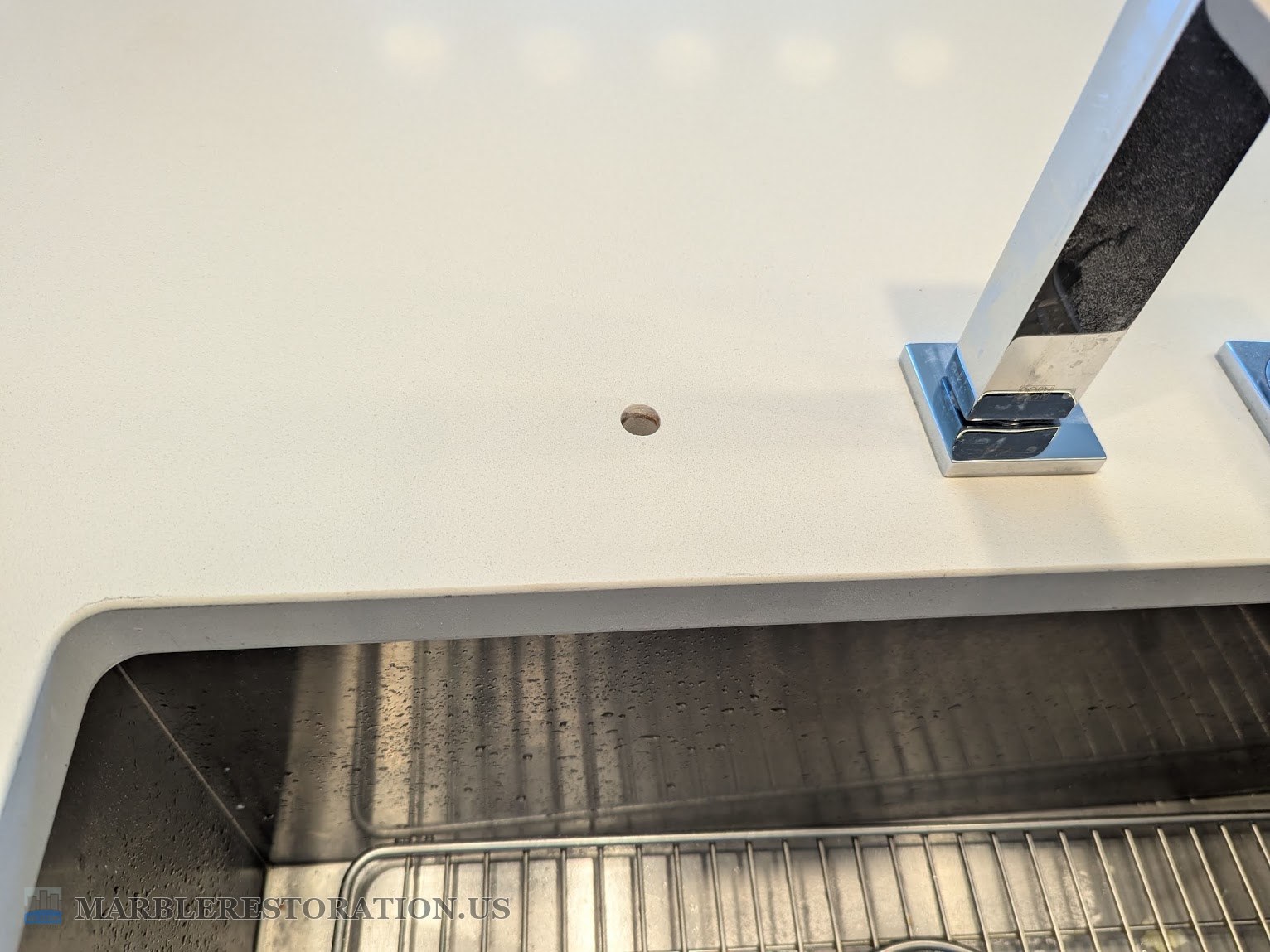 The drilled hole in the quartz countertop A round drilled hole in a white quartz countertop near the sink edge, with the main faucet base behind it